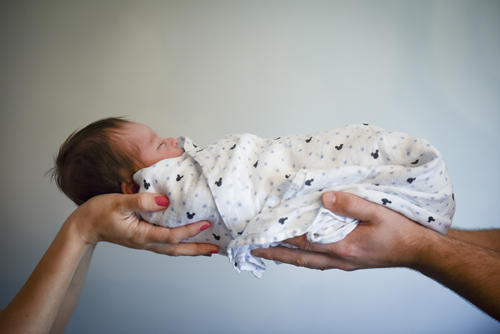 parents' hands supporting swaddled baby