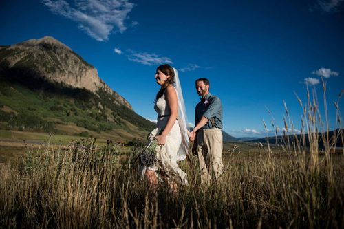 bride and groom walking through field near Colorado mountain