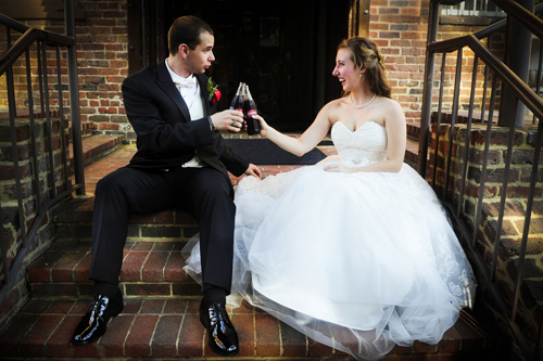 bride and groom sit on stairs and toast with a coke