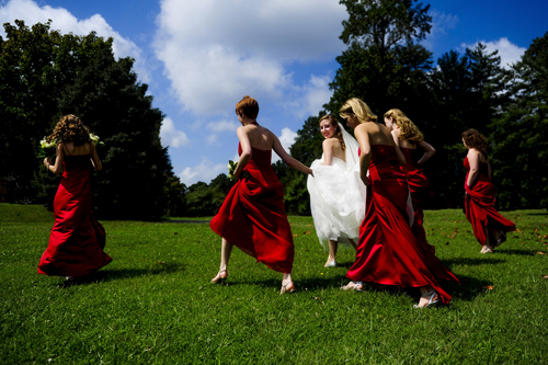 bride walking across grass with bridesmaids in red